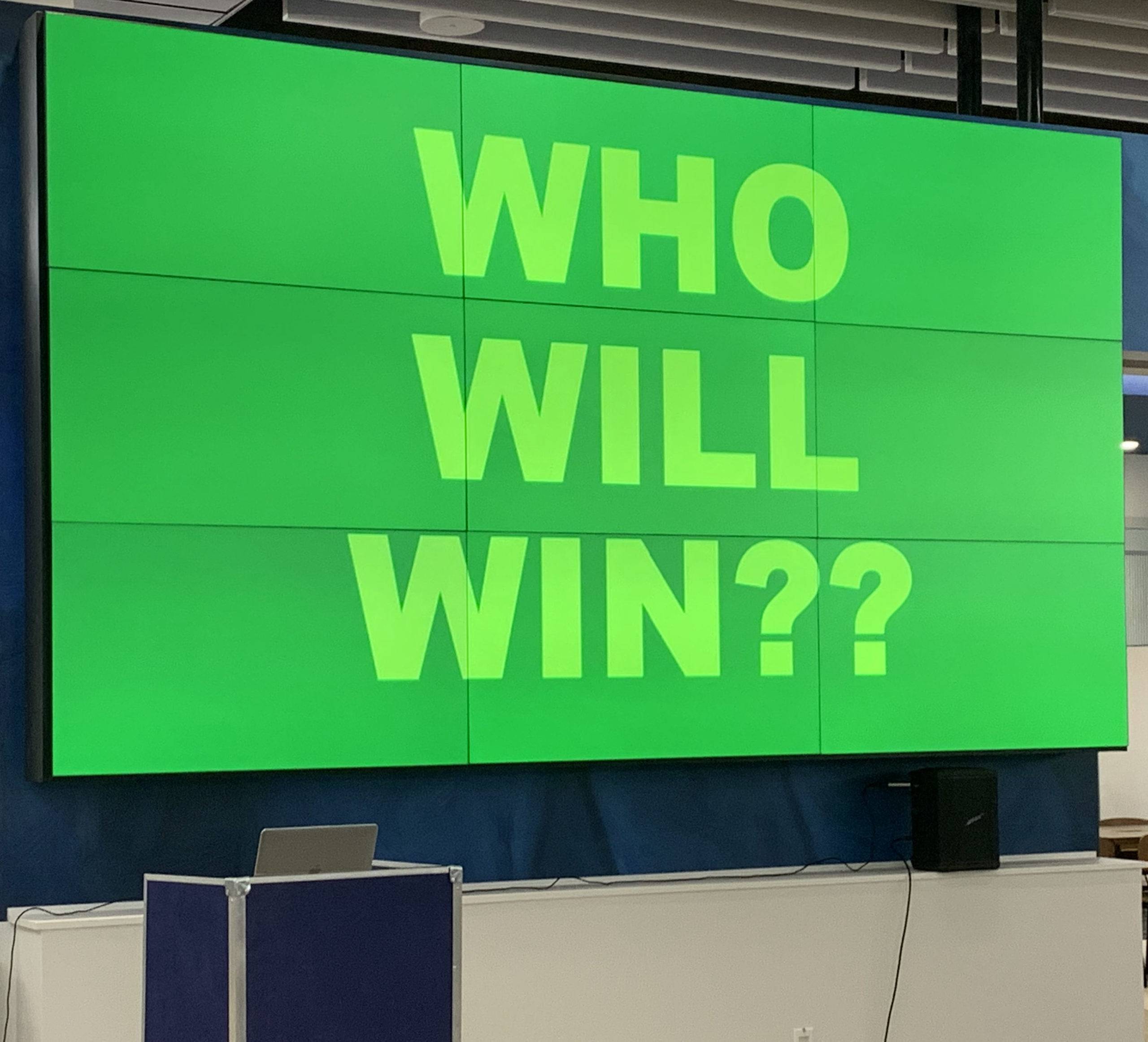 "Who will win" reads the large, green LED game show sign